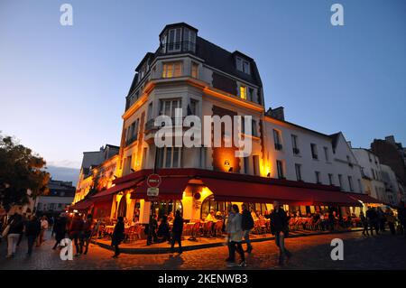 Fußgänger wandern in der Abenddämmerung auf dem Place du Tertre, einem Platz, der von Cafés gesäumt ist und von Straßenkünstlern im Pariser Viertel Montmartre besucht wird. Stockfoto