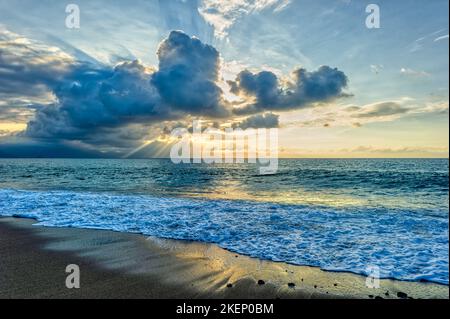 Ein Sonnenuntergang Am Meer Mit Sonnenstrahlen, Die Hinter Den Wolken Ausstrahlen Stockfoto