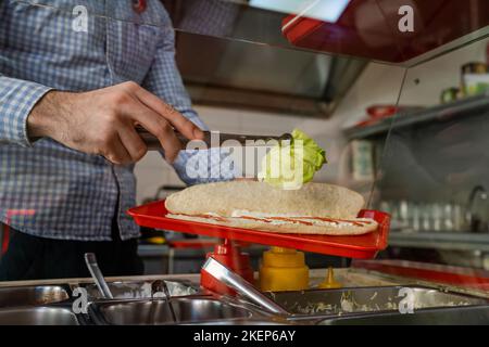 Nahaufnahme eines unbekannten kaukasischen Mannes, der im Fast-Food-Restaurant Sandwiches zubereitet und Salat zubereitet Stockfoto