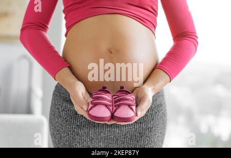 Schwangerschaft. Schwanger Frau erwartet Baby Mädchen hält rosa rote Schuhe im Geschlecht zeigen. Erwartet Mutter zeigt Baby Beule Bauch. Babykleidung Stockfoto