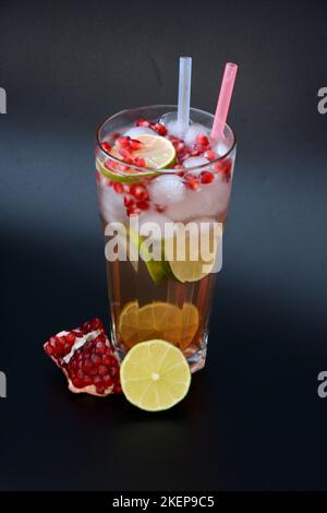 Limettensaft mit Granatapfelkernen in einem hohen Glas auf schwarzem Hintergrund mit Eis und Trinkhalmen. Vertikale Anordnung. Stockfoto