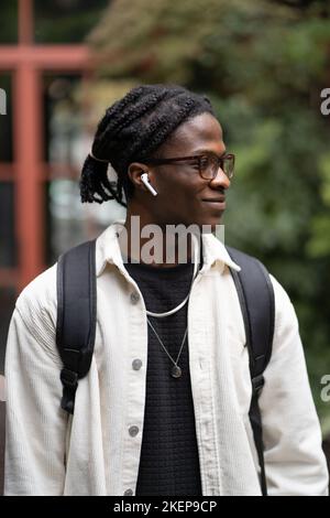 Mode optimistischer afroamerikanischer Mann, der mit Kopfhörern die Straße entlang läuft und Musik hört Stockfoto