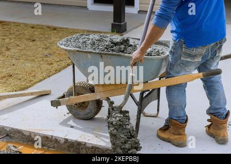 Bauarbeiter gießt Zement von Schubkarre auf, um einen neuen Bürgersteig an der Seite des Hauses zu schaffen Stockfoto