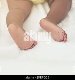 Diese Füße werden eines Tages große Fußabdrücke hinterlassen. Ein kleines Mädchen schläft zu Hause auf einem Bett. Stockfoto