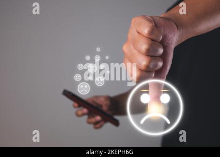 Evaluierungs- und Zufriedenheitskonzept. Die Hand zeigt den Daumen mit einem traurigen Emoji-Gesicht. Mittlere Nahaufnahme. Stockfoto