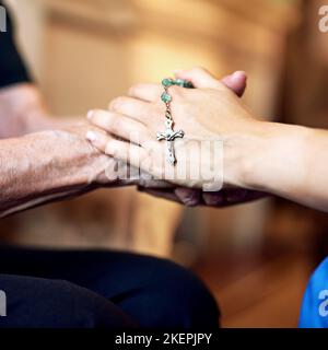 Durch den Glauben zusammengebracht. Eine Person, die barmherzig einen Rosenkranz hält, und eine ältere Frau, die Hände hält. Stockfoto