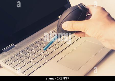 Computer mit Gebläsepumpe reinigen. Ein Mann bläst die Tasten auf der Tastatur mit einer Luftbirne Stockfoto