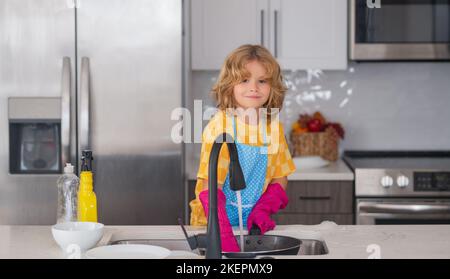 Spülkonzept. Kind macht und wischt Geschirr in der Küche. Kleines Kind putzt zu Hause. Kind, das Hausarbeit macht, hat Spaß. Nettes Kind Junge hilft Stockfoto