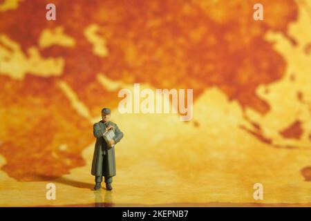 Miniatur Menschen Figur Spielzeug konzeptionelle Fotografie. Globaler Nachrichtenübergabedienst Ein militärischer Postbeamter, der einen Briefumschlag über dem Ohr hält Stockfoto