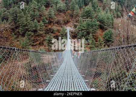 TTrekker überquert eine Metallhängebrücke in Nepal, Himalaya. Stockfoto