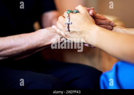 Lasst uns gemeinsam beten. Eine Person, die barmherzig einen Rosenkranz hält, und eine ältere Frau, die Hände hält. Stockfoto