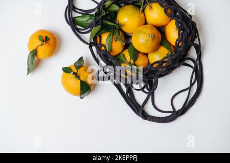 Unterpfote Mandarinen in einem Netzbeutel mit gewobenen Kordeln. Orange mit einem Hauch von Grün und einigen Blättern. Auf weißem Hintergrund. Stockfoto