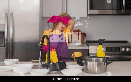 Wasch- und Reinigungskonzept. Müdes Kind, das im Kücheninneren Geschirr abwascht. Kind hilft bei der Hausarbeit. Housekeeping- und Hausreinigungskonzept Stockfoto