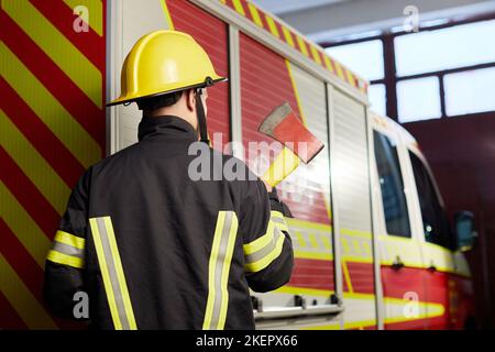 Feuerwehrmann voll ausgestattet mit Helm und Axt im Feuerwehrauto Hintergrund. Stockfoto