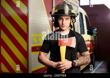 Foto von Feuerwehrmann mit Helm und Axt gegen Feuerwehrmann. Stockfoto