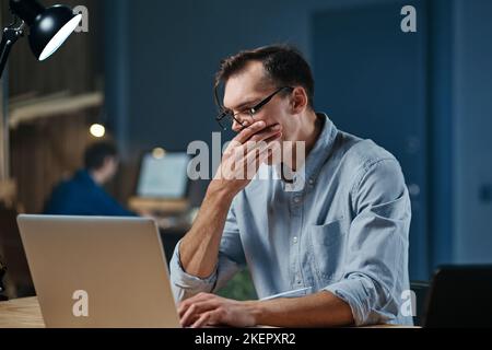 Müder Mann mit Laptop, der im Nachtbüro arbeitete. Stockfoto