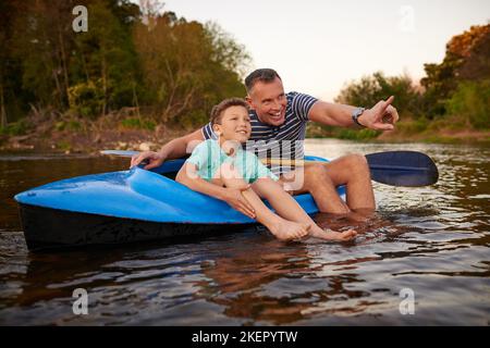 Wir gehen weiter flussabwärts. Ein Vater und ein Sohn sitzen in einem Ruderboot zusammen auf einem See. Stockfoto