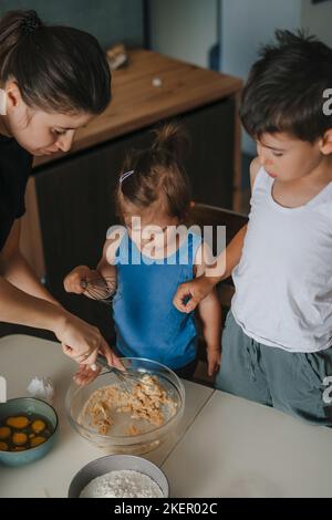 Fokussierte Mutter lernen Baby Mädchen mischen Zutaten in Schüssel. Mutter und ihre Kinder backen Plätzchen Kuchen und bereiten Pfannkuchen zum Frühstück zu Hause Stockfoto