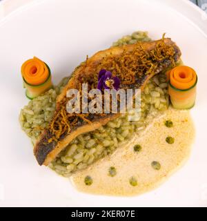 Rezept für gebratenes Seebarschfilet mit Kräuterrisotto, Weißweinsauce, Fresch-Creme, Karottenrolle und Zucchini-Streifen Stockfoto