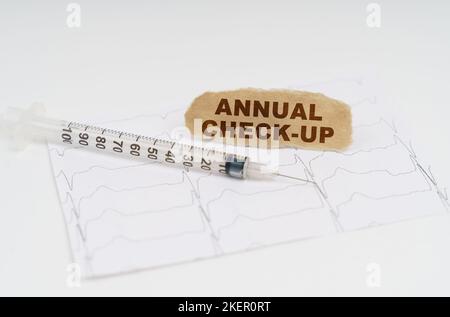 Medizin und Gesundheitskonzept. Auf dem Tisch befindet sich ein Kardiogramm, eine Spritze und Papier mit der Aufschrift - JÄHRLICHE ÜBERPRÜFUNG Stockfoto