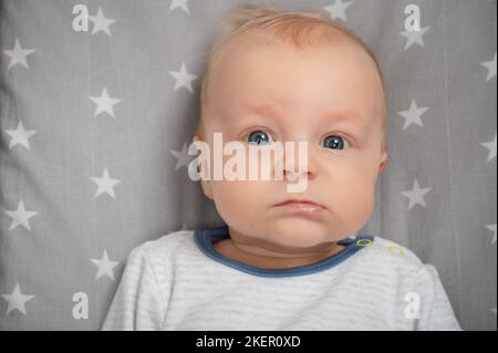Porträt eines schweren Neugeborenen, Nahaufnahme. Kind mit blauen Augen, Blick auf die Kamera. Gesichtsausdruck. Stockfoto