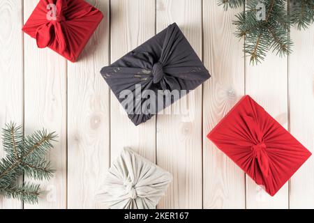 Komposition der weihnachtsgeschenke im furoshiki-Paket, Draufsicht. Fichtenzweige und Geschenkboxen auf weißem Brett. Objekt-Layout. Weihnachten oder Neu Stockfoto