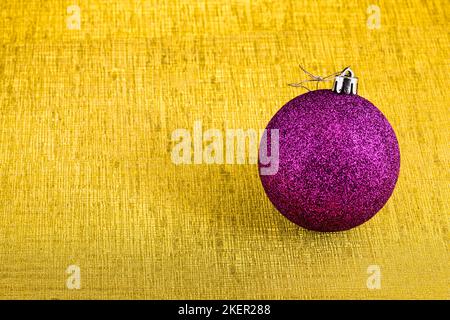 Eine lila weihnachtskugel mit Glitzer isoliert auf einem goldenen Hintergrund mit Textur. Stockfoto