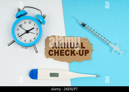 Medizinisches Konzept. Eine Uhr, ein Thermometer, eine Spritze und eine Pappe mit der Aufschrift - JÄHRLICHER CHECK-UP Stockfoto
