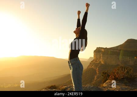 Seitenansicht Porträt einer eitrigen Frau, die bei Sonnenuntergang die Arme im Berg hochhebt Stockfoto