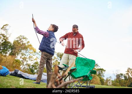 Ein Vater und ein Sohn, die zusammen ein Zelt aufschlagen, während sie zelten. Stockfoto