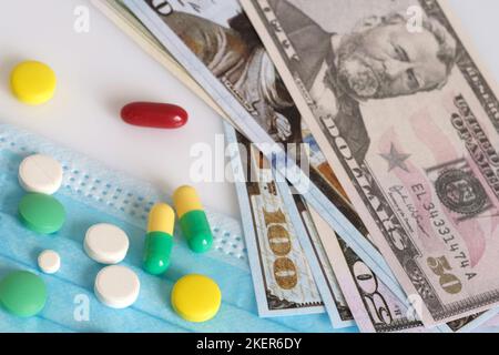 Dollar in einer medizinischen Maske, umgeben von Drogen und Pillen. Das Konzept von Medecine. Aufgenommen von oben auf weißem Hintergrund. Stockfoto