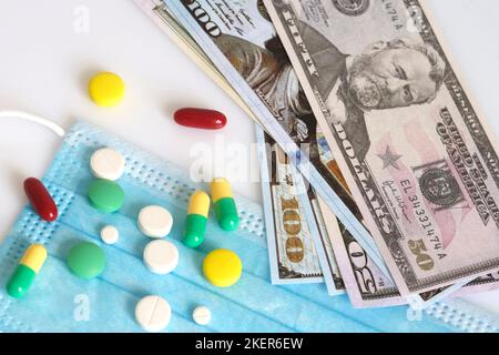 Dollar in einer medizinischen Maske, umgeben von Drogen und Pillen. Das Konzept von Medecine. Aufgenommen von oben auf weißem Hintergrund. Stockfoto