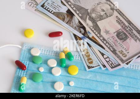 Dollar in einer medizinischen Maske, umgeben von Drogen und Pillen. Das Konzept von Medecine. Aufgenommen von oben auf weißem Hintergrund. Stockfoto