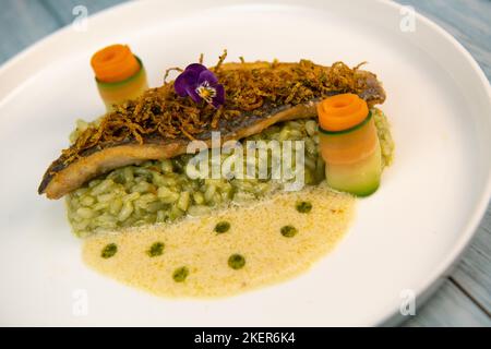 Rezept für gebratenes Seebarschfilet mit Kräuterrisotto, Weißweinsauce, Fresch-Creme, Karottenrolle und Zucchini-Streifen Stockfoto