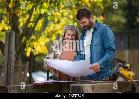 Glückliches reifes Paar mit Architekturentwürfen ihres zukünftigen Hauses, das im Freien steht. Stockfoto