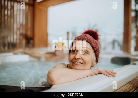 Ältere Frau genießt an kalten Wintertagen eine Badewanne im Freien auf der Terrasse. Stockfoto