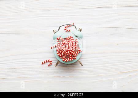 Weihnachtshintergrund mit Zuckerstöcken mit Wecker auf blauem Holzhintergrund. Stockfoto