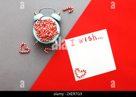 Weihnachtshintergrund mit Zuckerstöcken mit Wecker auf blaugrauem und rotem Hintergrund. Stockfoto