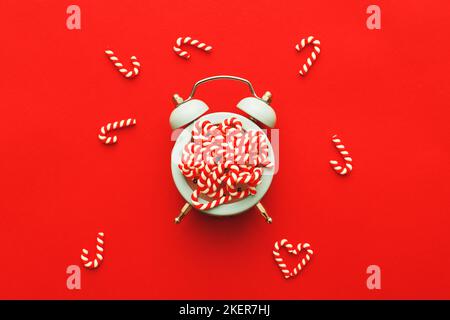 Weihnachtshintergrund mit Zuckerstöcken mit Wecker auf blaurotem Hintergrund. Stockfoto