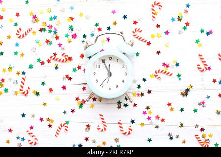 Weihnachtshintergrund mit Zuckerstöcken mit Wecker und bunten Pailletten auf blauem Holzhintergrund. Stockfoto