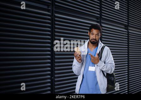 Junger Mann aus verschiedenen Rassen, der als Krankenschwester arbeitet und von der Arbeit zurückkommt und eine Tasse Kaffee hält. Stockfoto