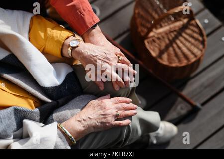 Draufsicht auf Senioren, die sich die Hände halten und einen romantischen Moment beim Herbstpicknickfahren in der Nähe des Sees haben. Stockfoto