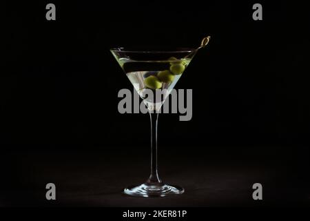 Glas des klassischen trockenen martini-Cocktails mit Oliven auf einem Tisch aus dunklem Stein vor schwarzem Hintergrund. Stockfoto