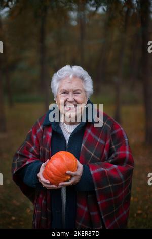 Ältere Frau mit Kürbissen im Herbstwald. Stockfoto
