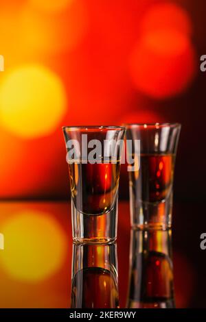 Zwei Gläser Whiskey oder Bourbon auf rotem Bokeh-Hintergrund. Whiskey-Stimmungskonzept Stockfoto