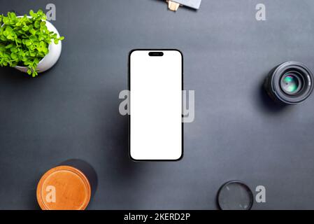 Telefon mit isoliertem Display schwebt über dem Schreibtisch. Die Frontkamera ist in das Display integriert. Moderne runde und dünne Kanten. Schwarzer Tisch mit Pflanze, le Stockfoto