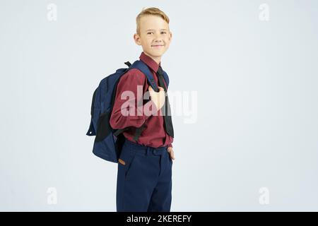 Ein Schuljunge hält einen Schulrucksack, steht seitlich, schaut auf die Kamera. Bildungskonzept Stockfoto