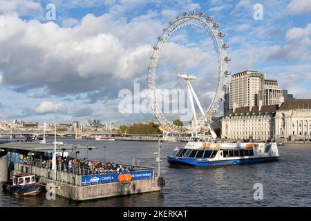 Ein City Cruises-Boot, das am Westminster Pier anlegt, mit Touristen und Besuchern, die darauf warten, an Bord zu gehen, und dem London Eye im Hintergrund. London Stockfoto