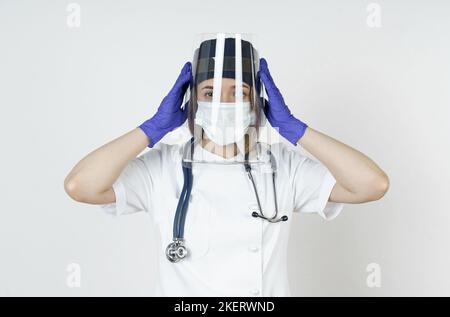 Medizin und Gesundheitskonzept. Porträt einer jungen Ärztin, die den Schutzschild von ihrem Gesicht entfernt. Isoliert auf weißem Hintergrund. Stockfoto