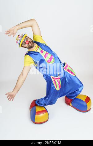 Urlaubskonzept. Der Clown ist ein Mann in einem leuchtend blauen und gelben Anzug, einer Brille und einem Hut, der emotional spielt. Stockfoto